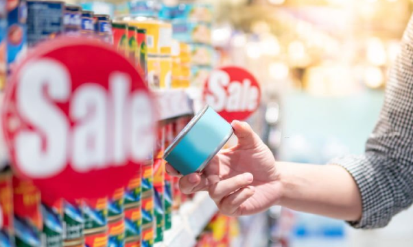 A customer trying to save money chooses cheap canned food from a supermarket or grocery store.