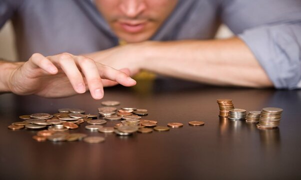 A man counts his coins on a tabletop to save money fast on a low income.