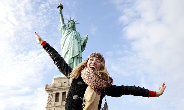 A happy woman taking photo at The Statue of Liberty in New York.